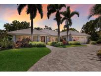 Stunning home showcasing palm trees, meticulous landscaping, and a paver driveway, set against a colorful sunset sky at 1780 Pine Harrier Cir, Sarasota, FL 34231