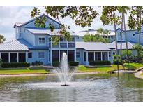 Water view of this gray two-story home, with a fountain, grassy lawn, and mature shrubbery at 1311 Siesta Bayside Dr # 1311-A, Sarasota, FL 34242