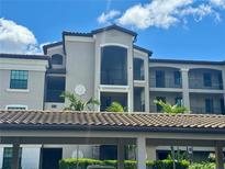 Low-angle view of condominium with portico, balconies, and Spanish-tile roof under bright blue sky at 16904 Vardon Ter # 201, Bradenton, FL 34211