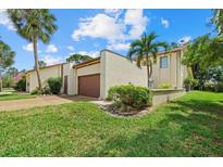 Beige exterior with a two-car garage and lush landscaping featuring a palm tree and vibrant green lawn at 6207 Courtside Dr # 23, Bradenton, FL 34210