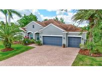Charming gray home with a brick driveway, complemented by lush landscaping and mature palm trees at 7705 55Th E St, Ellenton, FL 34222