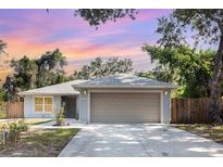 Charming single-story home featuring a two-car garage, well-manicured lawn, and mature trees against a lovely sunset at 1345 24Th St, Sarasota, FL 34234