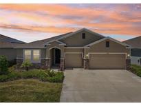 Charming single-story home with a two-car garage and stone accents under a beautiful orange sunset at 17536 Cantarina Cv, Bradenton, FL 34211