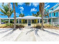 Charming yellow beach house with white trim, surrounded by palm trees and sandy landscape at 104 Magnolia Ave, Anna Maria, FL 34216