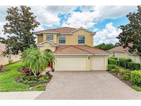 Two-story home featuring a tile roof, three-car garage, brick driveway, and professionally landscaped yard at 235 River Enclave Ct, Bradenton, FL 34212