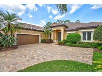 Charming tan home with a brick driveway, a tile roof, and lush landscaping with palm trees at 4818 88Th E St, Bradenton, FL 34211