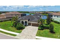 Stunning waterfront home featuring a tile roof, arched entryway, and lush tropical landscaping at 5622 Arnie Loop, Lakewood Ranch, FL 34211