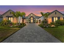 Stunning home exterior featuring lush landscaping, palm trees, brick driveway, and architectural design at sunset at 1182 Blue Shell Loop, Sarasota, FL 34240