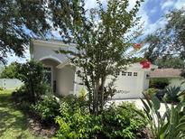 Charming home featuring a two-car garage, arched entrance, and lush landscaping with mature trees and flowering plants at 15207 Searobbin Dr, Lakewood Ranch, FL 34202