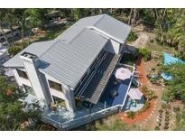 Stunning aerial view of the modern home, showcasing a metal roof, screened deck, manicured garden, and mature trees at 7251 Fish Farm Rd, Palmetto, FL 34221