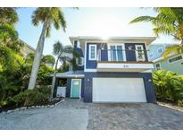 Two-story home with a blue facade, balcony, two car garage and lush, tropical landscaping at 211 65Th St, Holmes Beach, FL 34217