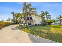 Charming stilt home with beautiful landscaping and a long driveway, surrounded by mature palm trees under a blue sky at 221 85Th St, Holmes Beach, FL 34217