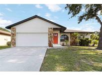 Charming single-story home featuring a red door, stone accents, and well-maintained landscaping at 2477 Wood Oak Dr, Sarasota, FL 34232