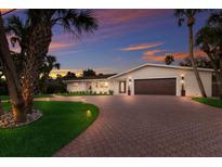 Charming home featuring a brick driveway, lush landscaping, and a two-car garage illuminated by a vibrant sunset at 5581 Shadow Lawn Dr, Sarasota, FL 34242