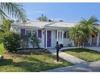 Charming single-story home featuring a white tiled roof, bright purple door and shutters, and lush landscaping at 730 Spanish S Dr # 99, Longboat Key, FL 34228