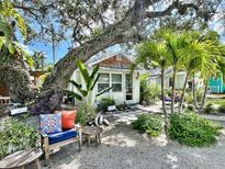 Charming cottage exterior featuring mature trees, lush tropical landscaping and inviting outdoor seating area at 4412 125Th W St, Cortez, FL 34215