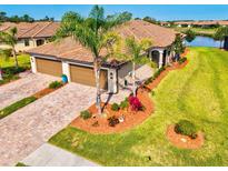 Beautiful home features a terracotta roof, two-car garage, paver driveway, tropical landscaping, and a lush green lawn at 12230 Amica Loop, Venice, FL 34293