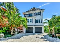 Inviting three-story beach house with a balcony and lush tropical landscaping at 5219 Calle Menorca, Sarasota, FL 34242