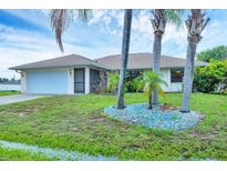 Charming single-story home with a two-car garage, lush green lawn, and mature palm trees at 408 Fletcher St, Port Charlotte, FL 33954