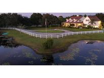 Picturesque property featuring a white-fenced home, pond with lily pads, and circular driveway at dusk at 20504 65Th E Ave, Bradenton, FL 34211