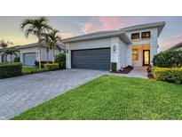 Inviting home featuring a paver driveway, dark garage door, manicured lawn, and tropical landscaping with palm trees at 5187 Barnett Cir, Bradenton, FL 34211
