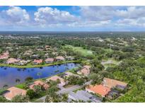 Stunning aerial view of a golf course community featuring a scenic pond, lush greenery, and beautiful homes with tile roofs at 7214 Marlow Pl, University Park, FL 34201