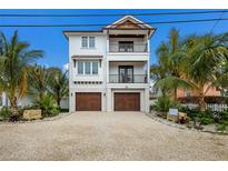 Coastal three-story home featuring double balconies, a two-car garage, and tropical landscaping at 2213 Avenue C, Bradenton Beach, FL 34217