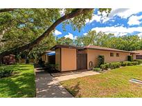 Inviting tan home with manicured lawn, decorative landscaping, and mature shade tree in a quiet neighborhood at 8472 60Th N St # 702, Pinellas Park, FL 33781