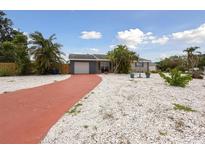 Charming single-story home with a red driveway, white rock landscaping, and vibrant tropical foliage at 4303 83Rd W St, Bradenton, FL 34209
