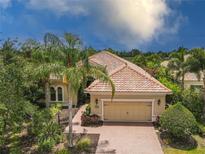Beautiful single-Gathering home with a manicured lawn, a tile roof, and a brick driveway leading to a two-car garage at 7542 Windy Hill Cv, Bradenton, FL 34202