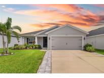 Charming single-story home featuring a well-manicured lawn and two-car garage, bathed in the warm hues of a vibrant sunset at 5958 164Th E Ave, Parrish, FL 34219