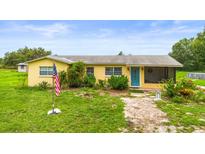 Charming yellow home features lush landscaping, vibrant blue door, and a welcoming screened porch at 5981 Jim Davis Rd, Parrish, FL 34219