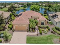 Beautiful tan home with a red tile roof, paver driveway, two car garage and lush landscaping on a lake at 673 Crane Prairie Way, Osprey, FL 34229