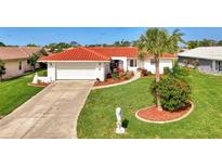 Charming single-story home featuring a red tile roof, a well-manicured lawn, and lush tropical landscaping at 74 Windsor Dr, Englewood, FL 34223