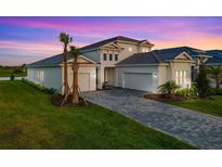 Beautiful home featuring a manicured lawn, brick driveway, and well-kept landscaping against a colorful sunset sky at 17128 Ranchside Pl, Lakewood Ranch, FL 34211