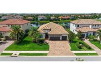 Beautiful tile roof home with a brick driveway, two car garage, and manicured green lawn with palm trees at 13220 Swiftwater Way, Lakewood Ranch, FL 34211