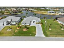 Waterfront home boasts lush lawn, mature palms, and an extended driveway leading to an attached two-car garage at 8106 Arlewood Cir, Port Charlotte, FL 33981