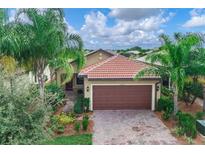 Charming home featuring a tile roof, lush landscaping, and a two-car garage at 13805 Posada St, Venice, FL 34293
