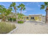Charming yellow home featuring tropical landscaping, a covered carport, and a white shell driveway at 627 Avenida Del Norte, Sarasota, FL 34242