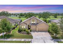 Charming tan house with a three-car garage, manicured lawn, and landscaping on a golf course at 9123 Raes Creek Pl, Palmetto, FL 34221