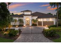 Elegant single-story home featuring a gated entrance, arched entryway, two-car garage, and lush tropical landscaping at dusk at 7211 Pasadena Gln, Lakewood Ranch, FL 34202