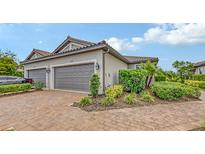 Home exterior featuring a two-car garage, brick driveway, beautiful landscaping, and tile roof at 10254 Morning Mist Ln, Sarasota, FL 34241