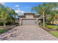 Charming home featuring a paver driveway and two-car garage, complemented by lush palm trees and well-maintained landscaping at 19023 Mangieri St, Venice, FL 34293