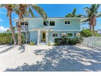 Charming two-story beach home with light blue siding, a yellow door, and lush palm trees at 733 Holly Rd, Anna Maria, FL 34216