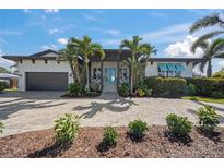 Beautiful single-story home featuring tropical landscaping, a brick driveway, and a covered entryway with charming blue doors at 5569 Cape Leyte Dr, Sarasota, FL 34242