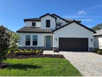 Charming two-story home boasts a well-manicured lawn, paver driveway, and stylish architectural details against a clear blue sky at 17134 Savory Mist Cir, Bradenton, FL 34211