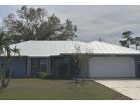 Charming single-story home with a lush lawn, a metal roof, mature landscaping, and an attached garage at 22321 Yonkers Ave, Port Charlotte, FL 33952