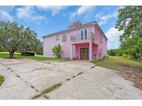 A pink two-story home with a unique roof design, concrete driveway, front balcony and landscaped yard at 4105 37Th E St, Bradenton, FL 34208