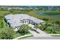 Stunning aerial view of a luxurious white home with a gray roof, surrounded by lush greenery and scenic waterways at 15315 Anchorage Pl, Lakewood Ranch, FL 34202