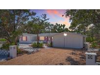 Charming single-story home featuring a white exterior, pink shutters, mature landscaping, and a spacious driveway at 5572 Shadow Lawn Dr, Sarasota, FL 34242